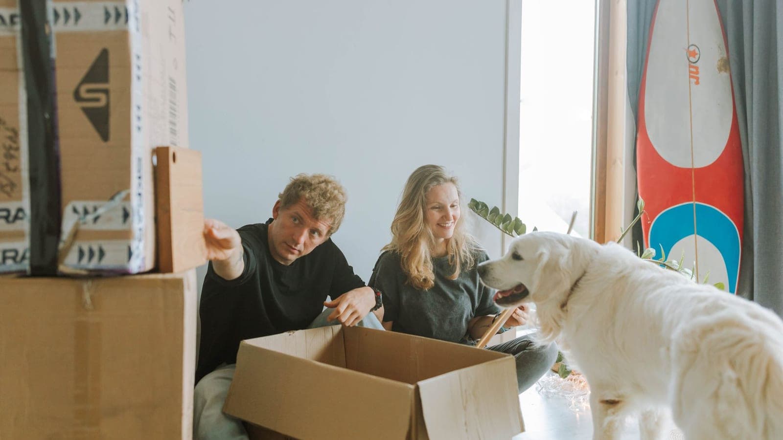 Couple unpacking moving boxes with their happy white dog beside them after moving cross country with pets